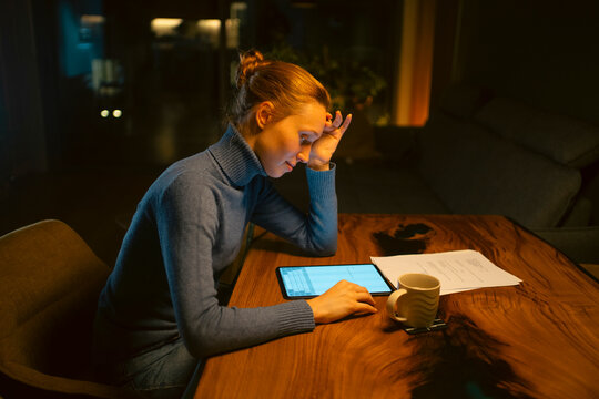 Woman working on tablet late at night feeling stressed
