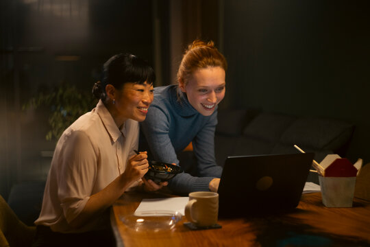 Colleagues working late on laptop eating takeout food
