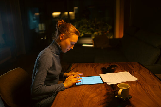 Woman working focused on tablet at night home