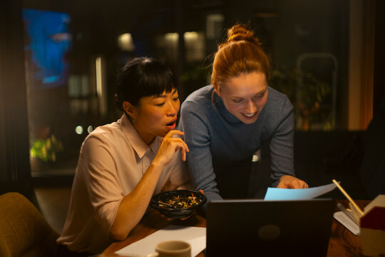 Diverse women collaborating on a laptop at night, working late