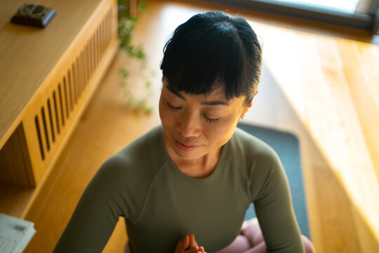 Asian woman meditating at home finding moment of calm