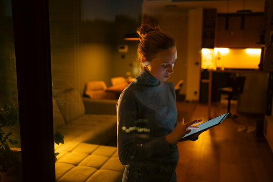 Woman using modern smart home technology tablet at night
