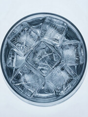 Frozen ice cubes sit in a clear glass filled with water on a light background