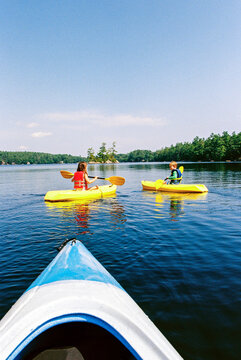 Two kids paddling kayaks in a Maine lake in summer