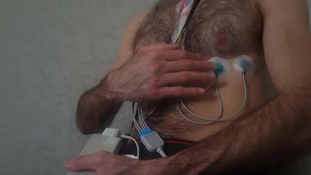 Adult male connecting ECG electrodes on chest at home for heart rate monitoring, healthcare technology concept, medical testing, cardiology screening, self care lifestyle.