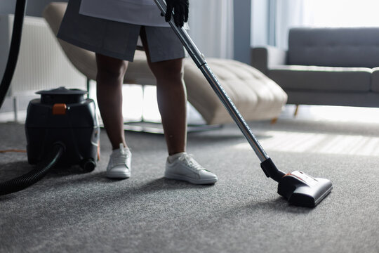 Cropped view of maid vacuuming floor in blurred hotel room at daytime