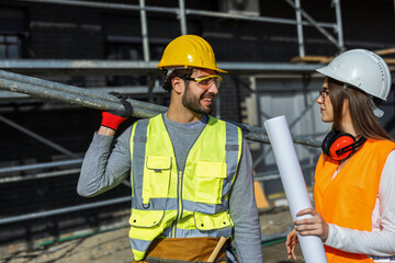 Male and female engineers holding blueprints and talking at construction site