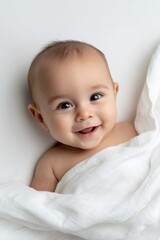 Smiling hispanic baby wrapped in white blanket against soft background