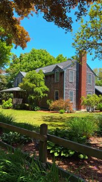 Classic New England shingle style house with brick chimney. Two story residential home with natural wood shingles and lush green landscape.