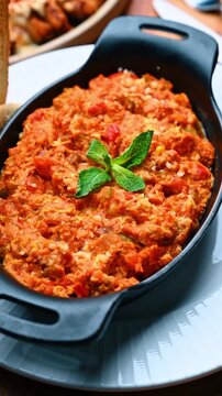 Close up of traditional menemen eggs with tomato and mint. Factual view of red scrambled eggs with vegetables in a black dish served on a white plate with toast.