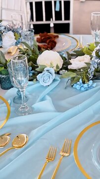 Elegant wedding table decor with blue runner and gold. Detailed view of formal table setting featuring blue glassware gold cutlery and white floral centerpieces