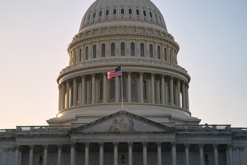 Fototapeta premium Last beams of golden sunlight on the United States Capitol Building in Washington, DC, with the American flag waving. Dramatic view