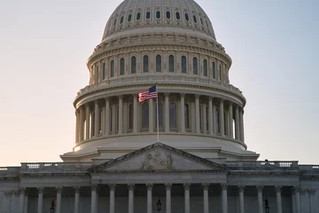 Last beams of golden sunlight on the United States Capitol Building in Washington, DC, with the American flag waving. Dramatic view © berezko