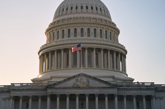 Last beams of golden sunlight on the United States Capitol Building in Washington, DC, with the American flag waving. Dramatic view