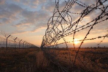 Barbed wire fence under a dramatic sunset sky