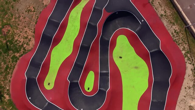 Top-down aerial view of a colorful asphalt pump track with flowing berms and rollers, showcasing geometric layout and purpose-built design for bikes and skateboards