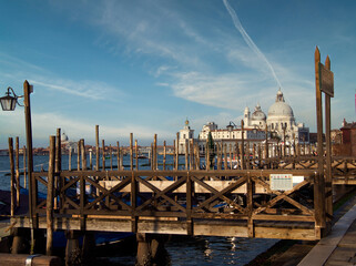 A picturesque view of the iconic Santa Maria della Salute church and Punta della Dogana across the water, framed by a rustic wooden gondola pier in the foreground. © jmag.foto