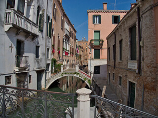 Traditional gondola carrying a couple, being navigated by a gondolier under an arched stone bridge on a narrow residential canal surrounded by historic buildings. © jmag.foto