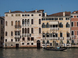 Naklejka premium Grand Canal Palaces Facades on a Clear Day - A row of historic Venetian palazzi facades along the Grand Canal with arched windows, balconies, and water access points under a clear sky.