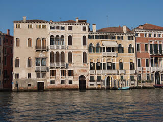 Fototapeta premium Grand Canal Palaces Facades on a Clear Day - A row of historic Venetian palazzi facades along the Grand Canal with arched windows, balconies, and water access points under a clear sky.