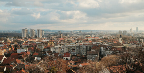 Obraz premium Wide city panorama from Gardos Tower showing Belgrade residential rooftops and distant high rise buildings beneath layered clouds.