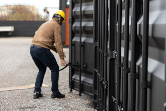 Worker opening black shipping container door in logistics yard