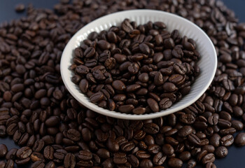 Fototapeta premium Roasted coffee beans in a white ceramic bowl on a dark background, top view.