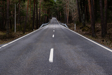 Obraz premium Long straight mountain road surrounded by trees, photographed from the center of the asphalt. No vehicles present, creating a strong sense of direction, perspective and depth.