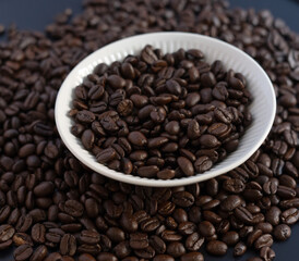 Fototapeta premium Roasted coffee beans in a white ceramic bowl on a dark background, top view.