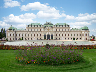 Fototapeta premium Upper Belvedere Palace and Formal Gardens - Stunning Baroque facade of the Oberes Belvedere reflected in the water basin with vibrant flowers in the foreground on a sunny day.