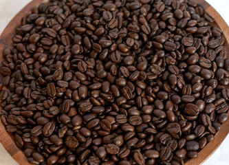 Fototapeta premium Close up of roasted coffee beans in a wooden bowl on a light surface.