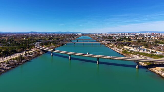 Aerial view of the Turia River flowing toward the Mediterranean Sea in Valencia, showing bridges, turquoise water, urban landscape, and coastal infrastructure