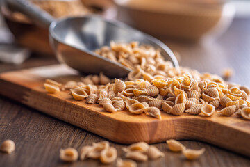 Wholegrain conchiglie pasta on scoop on wooden table.