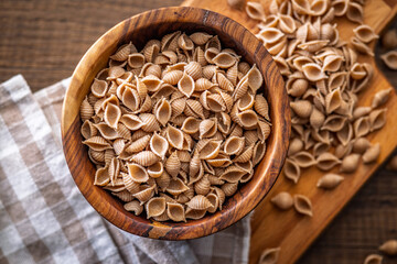Wholegrain conchiglie pasta in bowl on wooden table. Top view.