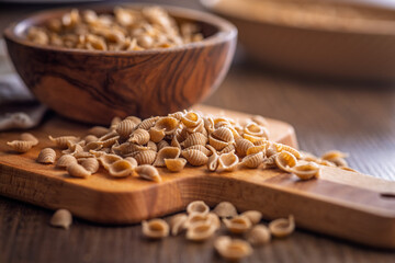 Wholegrain conchiglie pasta on wooden table.