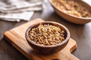 Wholegrain conchiglie pasta in bowl on wooden table.