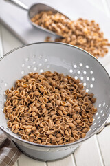 Wholegrain conchiglie pasta in colander on white table.