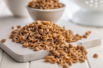 Wholegrain conchiglie pasta on white table.