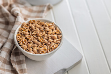 Wholegrain conchiglie pasta in bowl on white table.