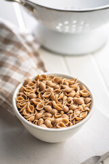 Wholegrain conchiglie pasta in bowl on white table.