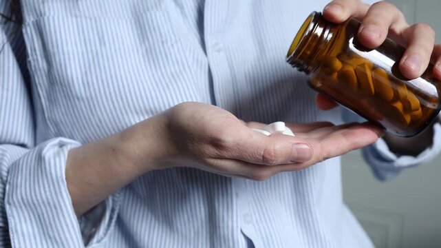 Woman pouring pills from small brown glass jar to a hand. Taking medication at home, disease prevention, taking antidepressants, vitamins, dietary supplements. Healthcare and medicine.