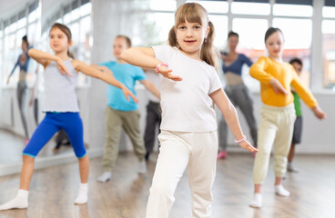 Fototapeta premium Girls with boys repeat teaches sequences of movements during training, train to perform electro dance, enjoys active hobby to favorite music. Unrecognizable female teacher administer conduct class