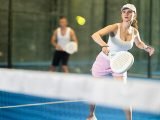 Active woman with racket training on indoor court playing padel game and hitting ball