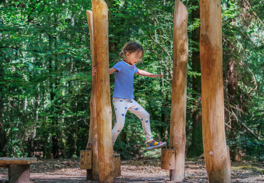 Girl balancing on wooden posts in forest playground at summer