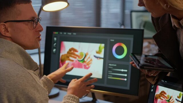 Caucasian man gesticulating while explaining problems of image and its editing problem to blonde producer with tablet in hands
