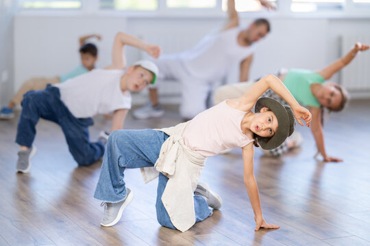 Emotional tween girl mastering krump dance routines during lively group session in children dance studio, guided by passionate male teacher..