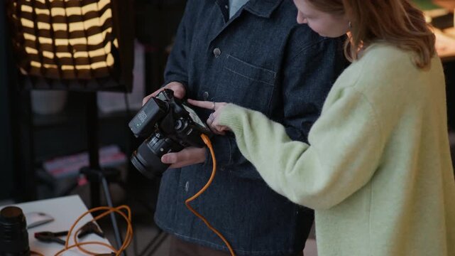 Professional photographer showing camera display with photo of brand new cosmetics while designer looking at it and adjusting props on table