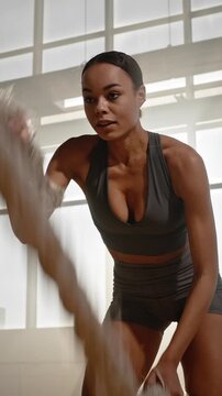 Steadicam shot of motivated young fitness woman exercising with battle rope in abandoned warehouse.