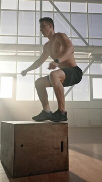 Determined shirtless male athlete strengthen legs and buttocks muscles, jumps up on box. Slow motion