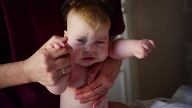 Caregiver supporting a baby upright while holding their hands. Early development and physical support during infancy